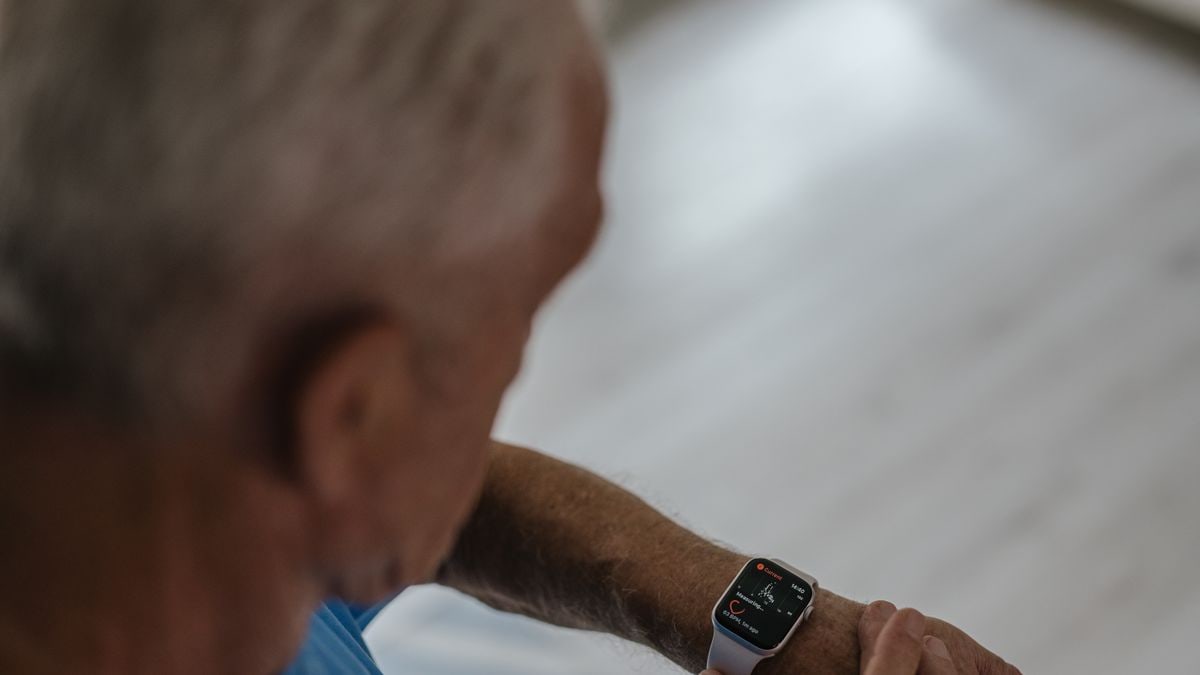 A senior man interacts with a smartwatch indoors, focusing on technology and lifestyle.